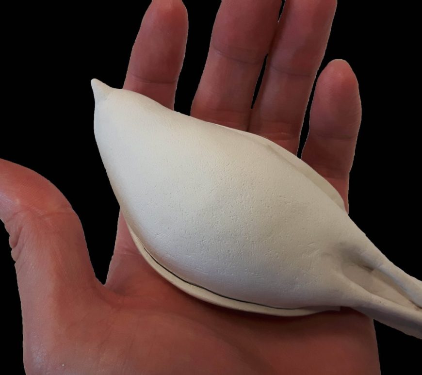 A hand holds a bird sculpture made of white clay. The hand belongs to a white male