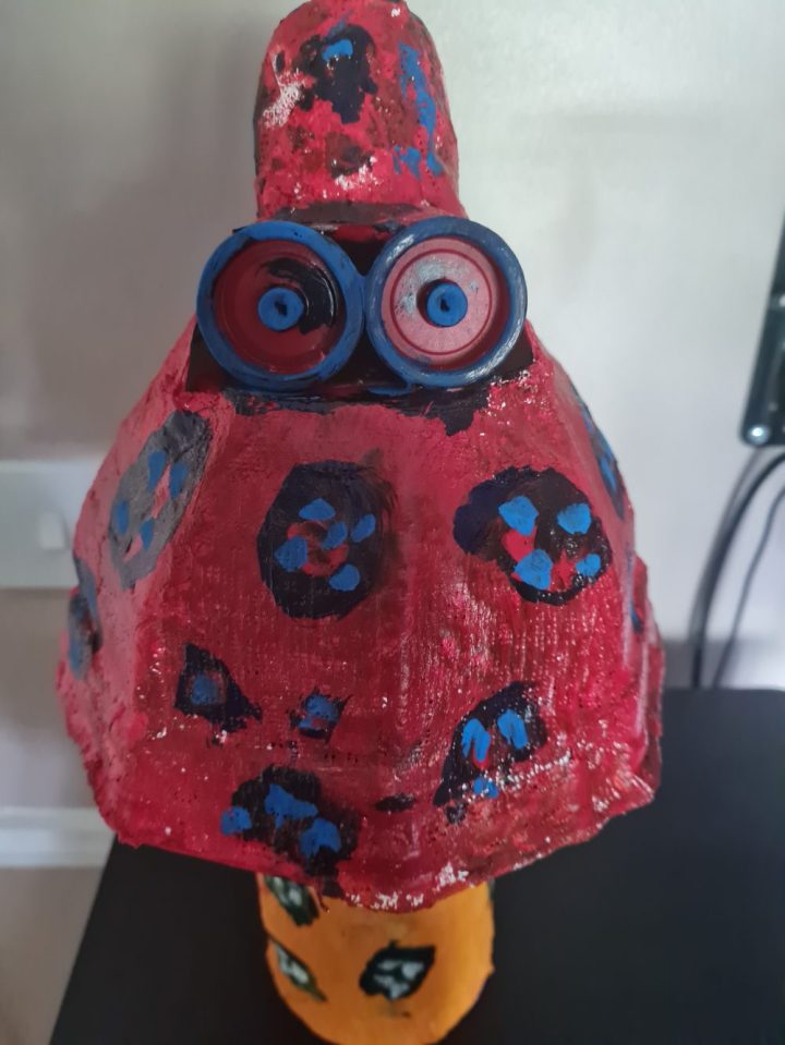 Protest plastics sculpture by Alex. A mushroom shape in pink and orange with plastic bottle-cap eyes