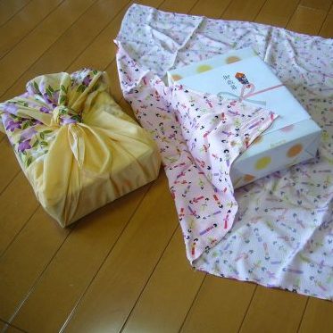Two gifts sit on a wooden surface. One is open and sat on a square of fabric, the other is wrapped in fabric
