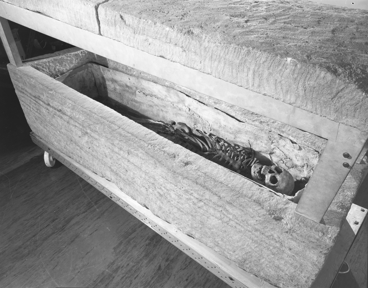 Photograph of a stone coffin with lid with human skeleton inside