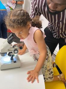 Image of a child looking down a microscope with the help of her father