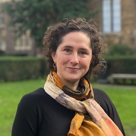 Adria LeBoeuf, smiling, wearing an orange scarf and black top, standing in a garden.